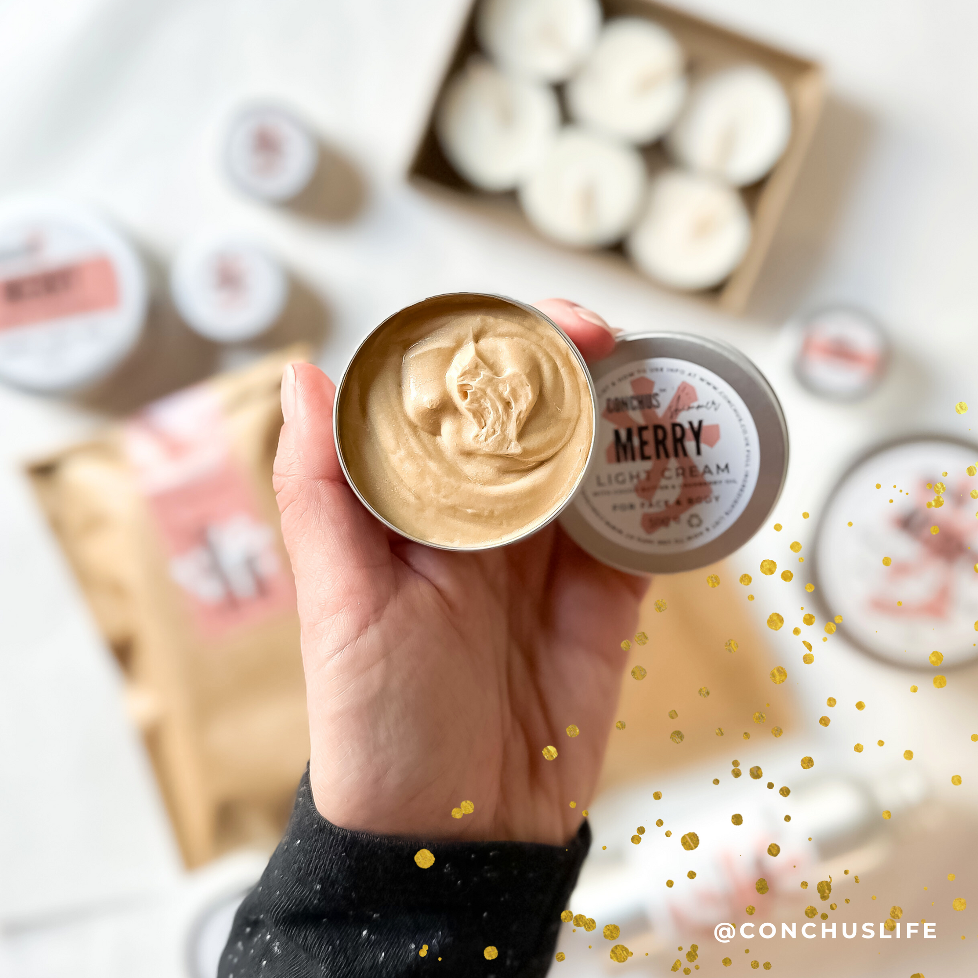 Open tin of CONCHUS MERRY Light Cream Shimmer held above festive CONCHUS packaging.