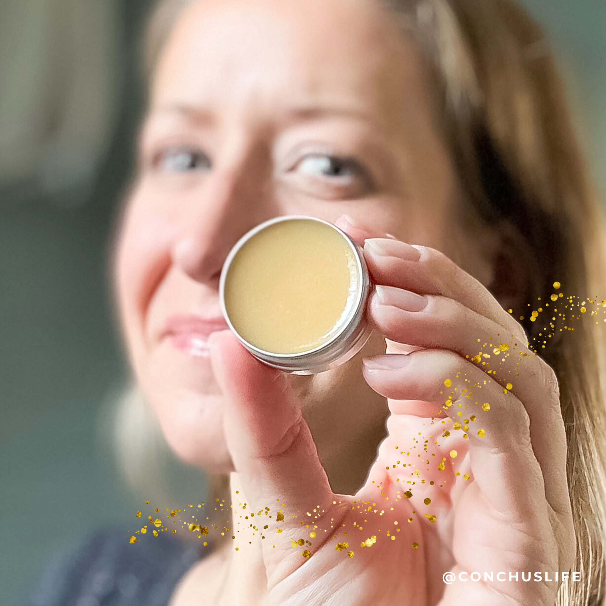 Person holding open tin of CONCHUS MERRY Lip Gloss showing glossy smooth texture