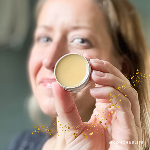 Person holding open tin of CONCHUS MERRY Lip Gloss showing glossy smooth texture