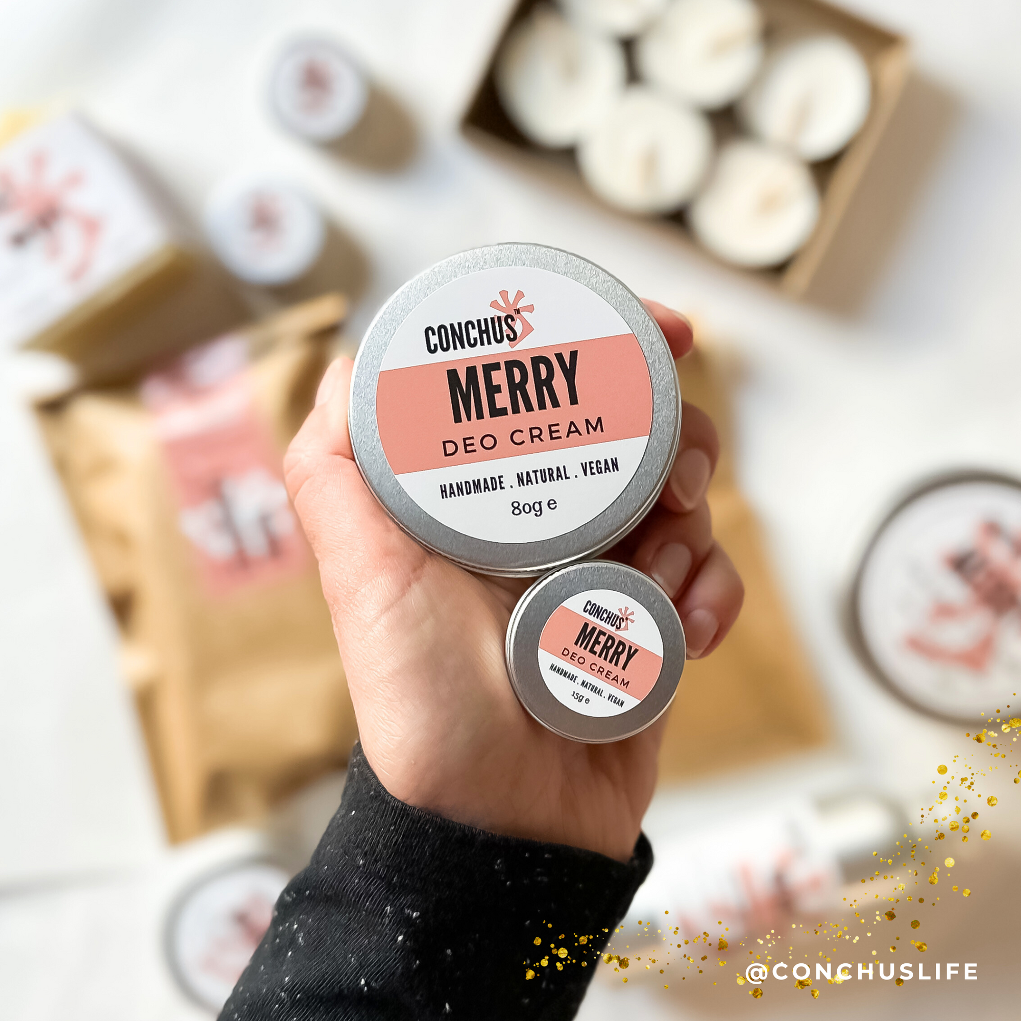 Open tin of CONCHUS MERRY Deo Cream held above CONCHUS packaging and gift items.