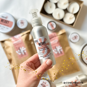 CONCHUS MERRY Light Oil bottle held over festive packaging and skincare gift items. Gift ideas for her. Gift ideas for Mum. 