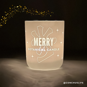 Lit CONCHUS MERRY Botanical Candle glowing through etched design in dark room