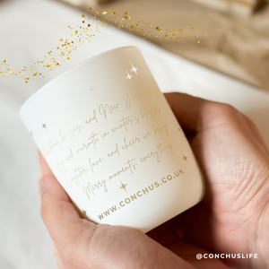 Person holding CONCHUS MERRY Botanical Candle showing festive etched poem on the back of the vessel